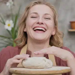 Mama Lila, a joyful plus-size woman and co-author at Feel the Recipes, laughing as she kneads dough in her sunlit, rustic kitchen.