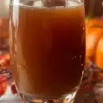 Bottles of homemade cider on a wooden table surrounded by fresh apples