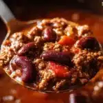 A steaming bowl of the best chili recipe garnished with fresh herbs.