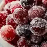 A bowl of bright red sugared cranberries ready to serve as a festive treat.