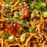 Plate of sticky garlic chicken noodles garnished with green onions