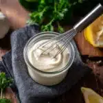 Homemade garlic aioli in a bowl with fresh garlic and herbs.
