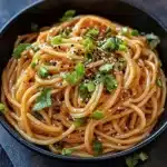 Bowl of Korean style spicy garlic noodles garnished with herbs and chili flakes